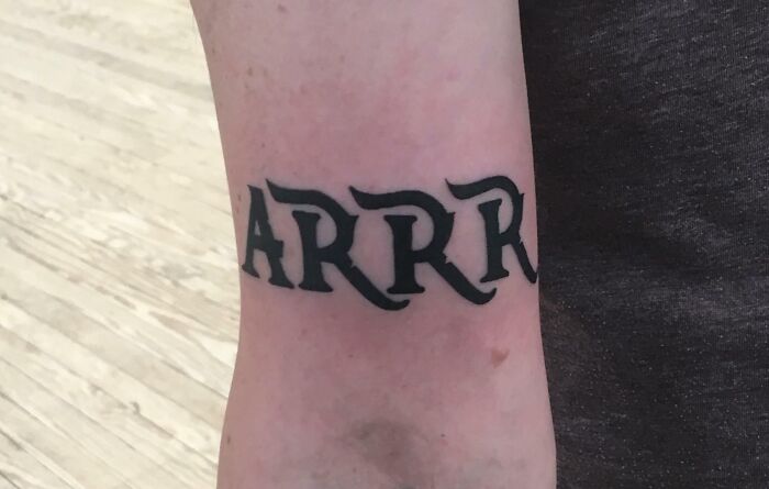 Arm tattoo with the word "ARRR" in bold black letters on light skin.