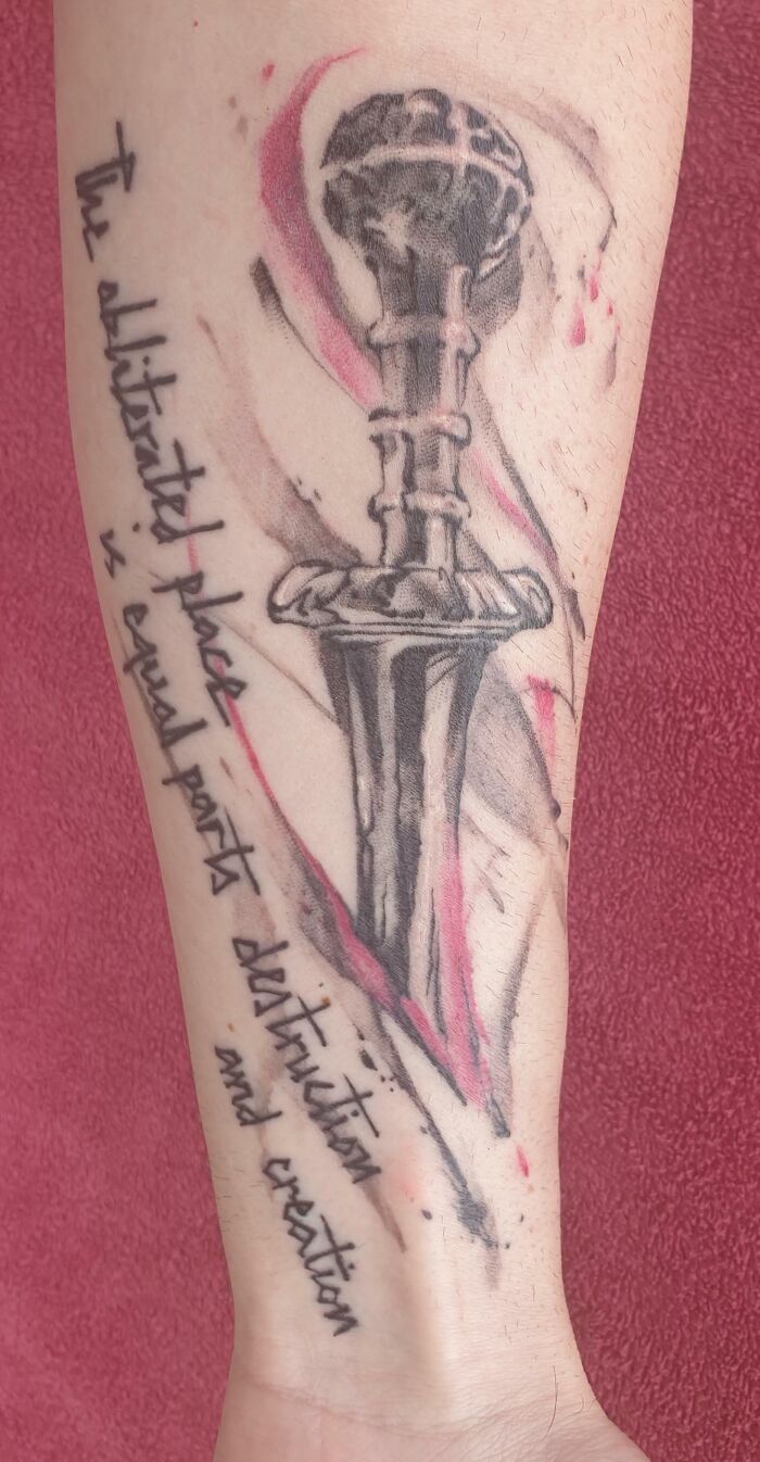 Sword tattoo with artistic writing on forearm, blending black and red ink, symbolizing destruction and creation.