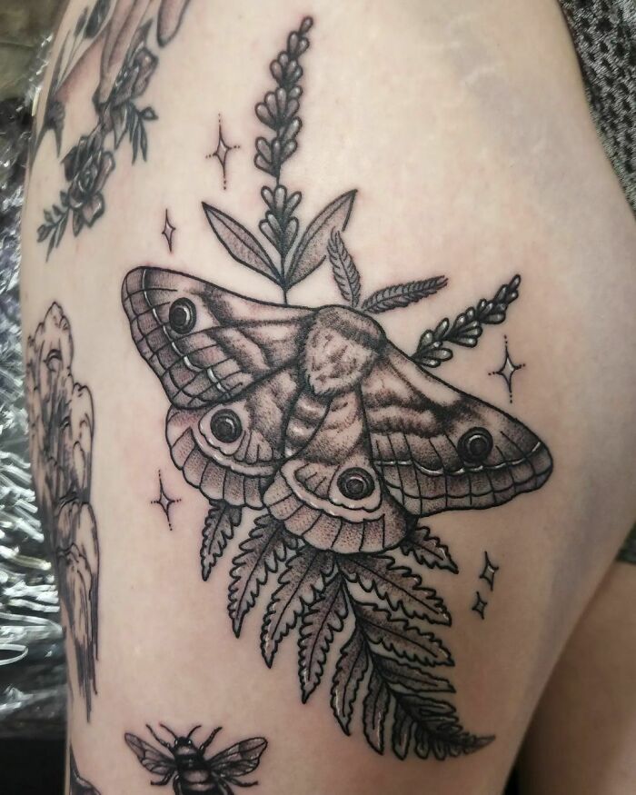Moth-inspired nature tattoo with fern and floral details, featuring intricate shading and line work.