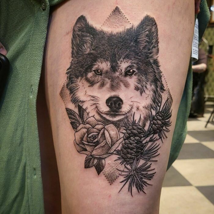 Wolf nature tattoo featuring floral and pine cone details on a person's thigh.