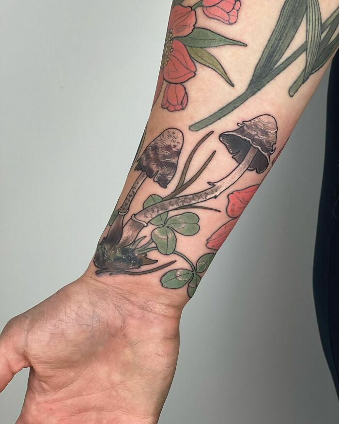 Nature tattoo with mushrooms, clover, and flowers on a person's forearm.