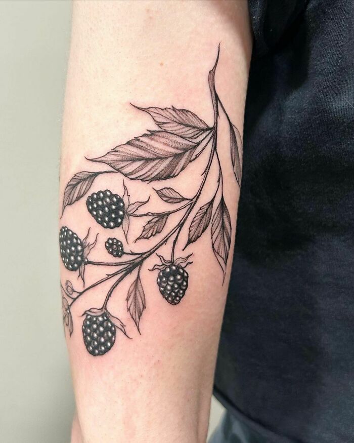 Nature tattoo of a blackberry branch on an arm, featuring detailed leaves and berries.