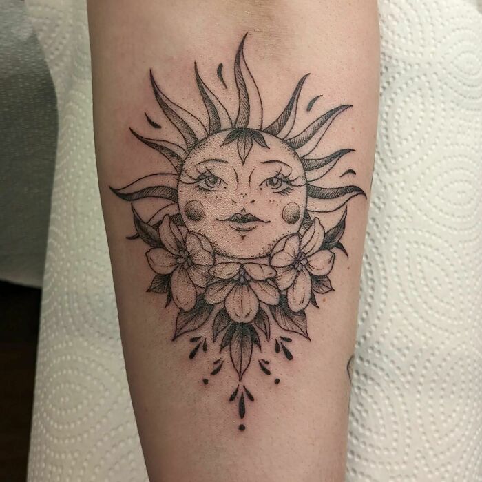 Nature tattoo featuring a stylized sun with floral details on forearm.