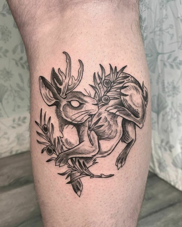 Black ink jackalope nature tattoo with leaf details on leg.