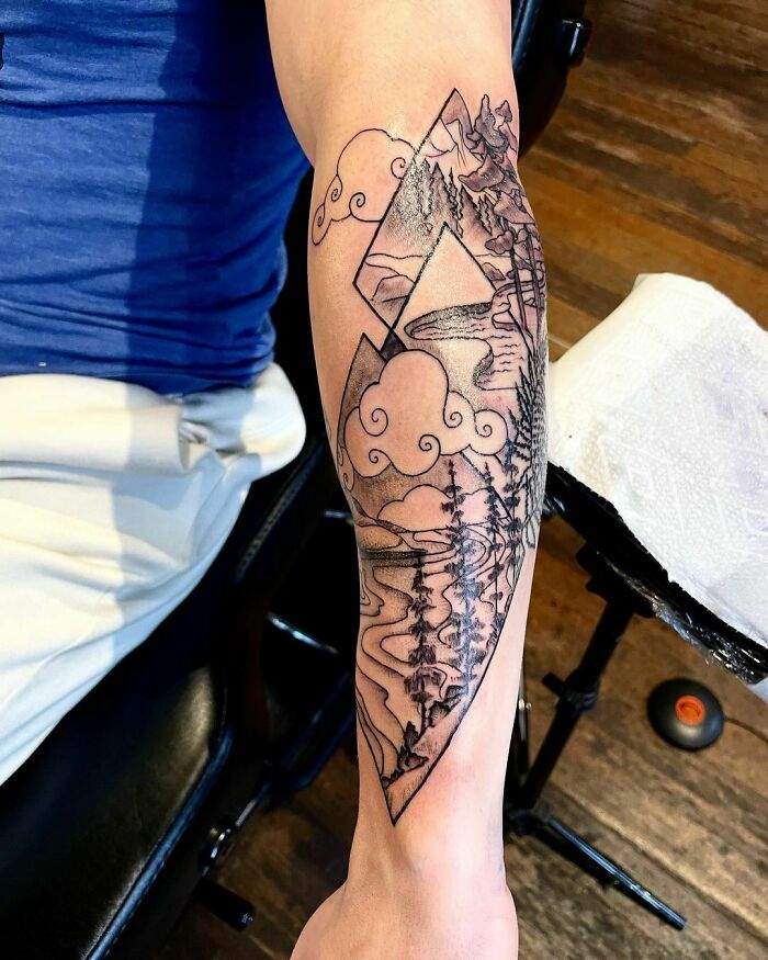 Nature tattoo depicting mountains, trees, and clouds in geometric shapes on a forearm.