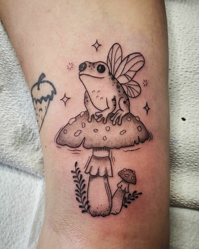 Fairy frog sitting on a mushroom nature tattoo, showcasing unique and whimsical elements.