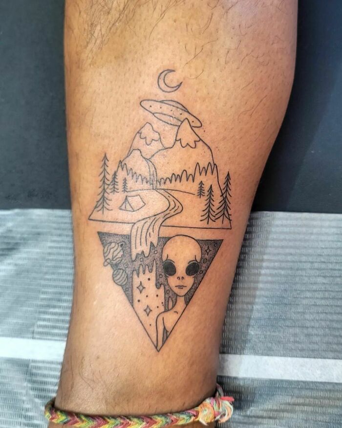 Nature tattoo featuring mountains, trees, and an alien design on a leg.