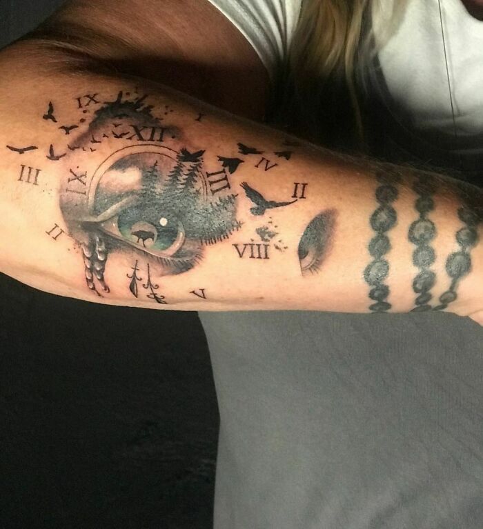 Nature tattoo featuring trees, birds, and clock elements on a person's arm.