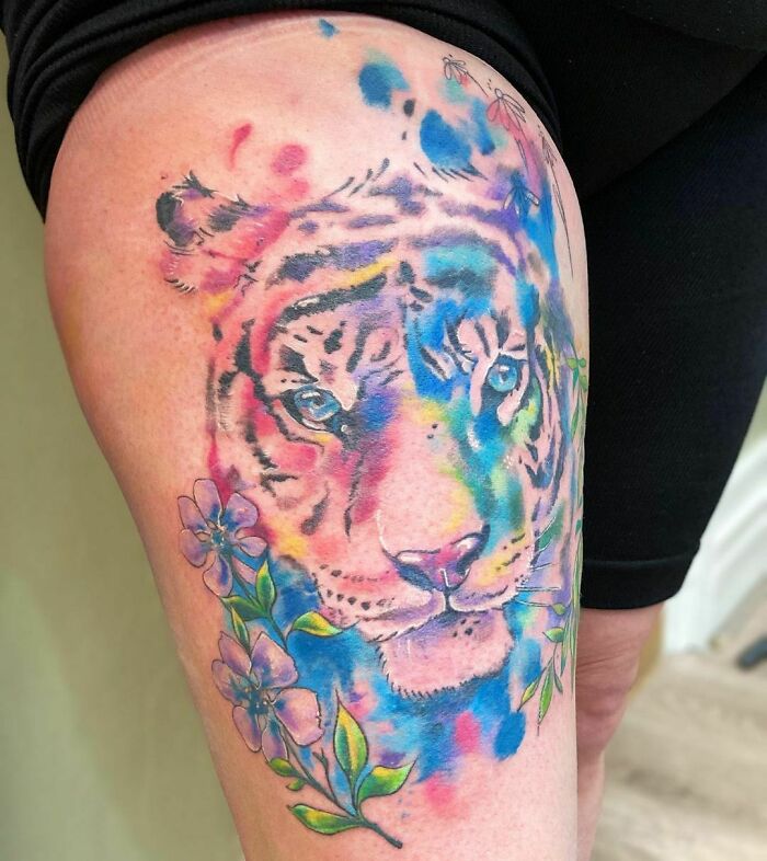 Colorful tiger nature tattoo with floral elements on thigh.