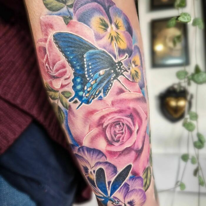 Colorful nature tattoo with a blue butterfly and pink roses on a person's arm, showcasing a wild side.