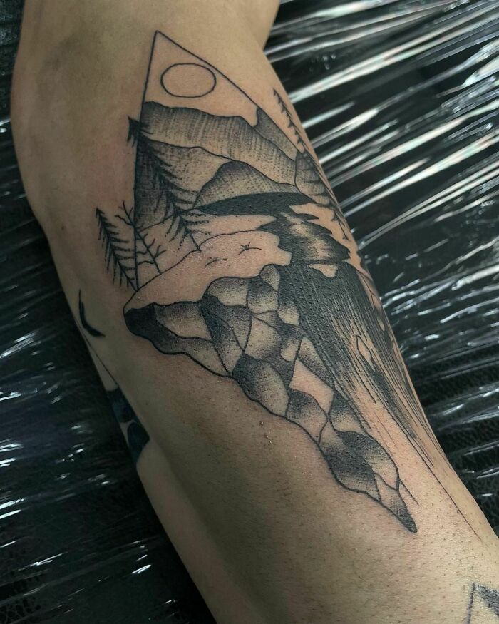 Nature tattoo featuring mountains, trees, and river, symbolizing a wild side.