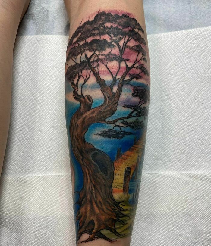 Nature tattoo of a winding tree against a colorful sunset sky on a forearm.