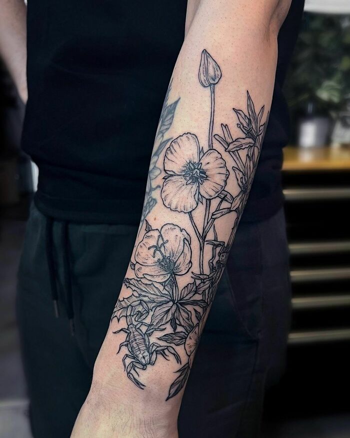 Arm showcasing an intricate nature tattoo with flowers and scorpion, symbolizing a wild side.