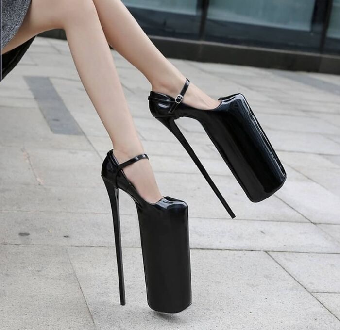 Black high-heeled platform shoes with extremely tall, thin heels, showcasing a unique and weird footwear design.