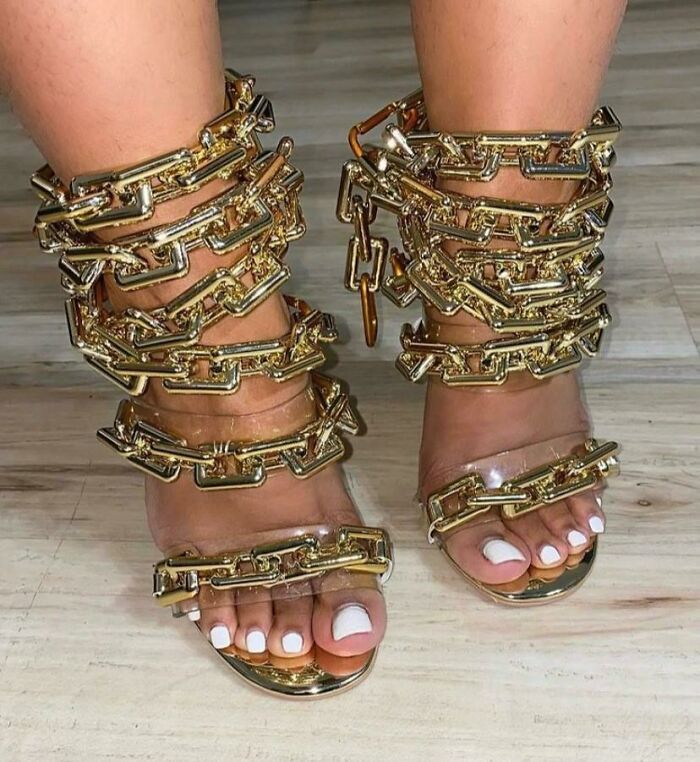 Unique shoes featuring chunky gold chain design on a wooden floor.