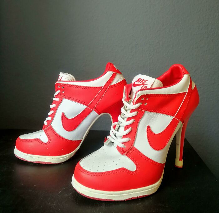 Weird shoes designed as red and white Nike high heel sneakers on a dark surface.