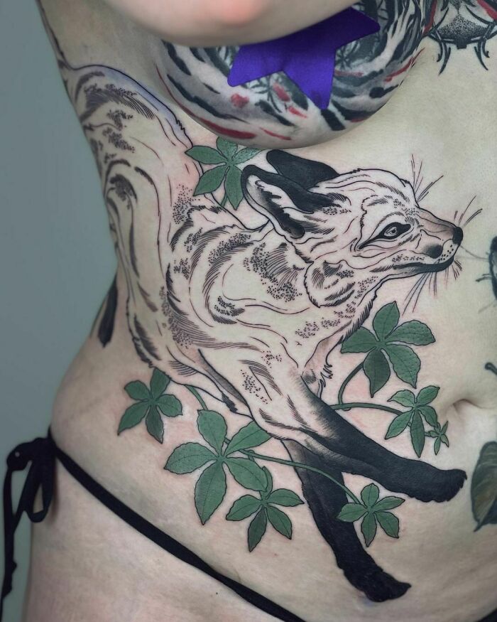 A fox design tattoo on skin with green leaves, showcasing a nature-inspired theme.