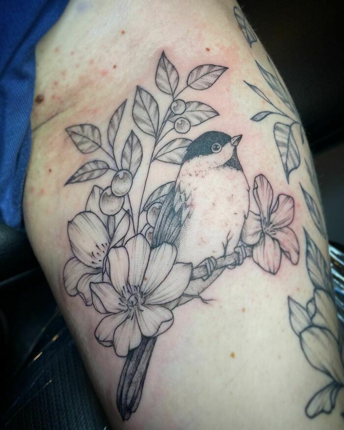 Black-and-white nature tattoo of a bird and flowers on skin.
