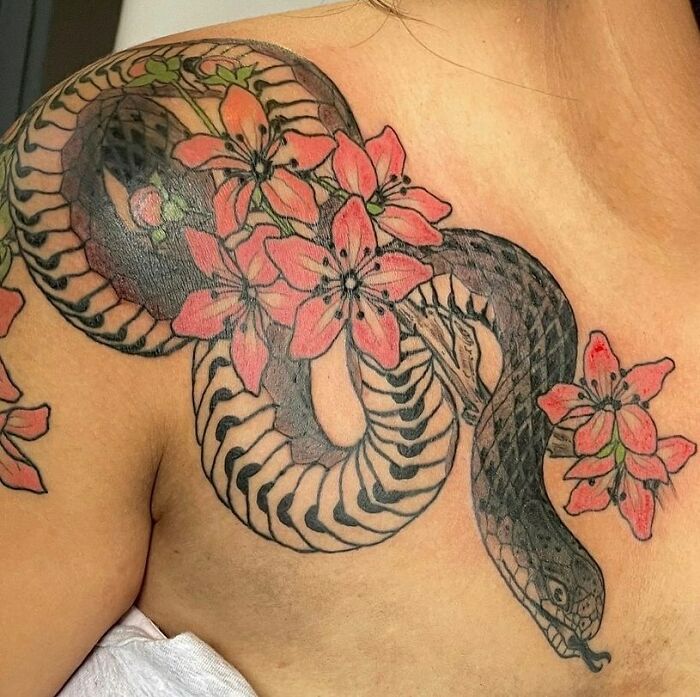 Nature tattoo featuring a snake intertwined with red flowers on shoulder.