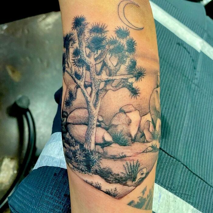 Nature tattoo featuring a desert landscape with a tree, rocks, and a crescent moon on an arm.