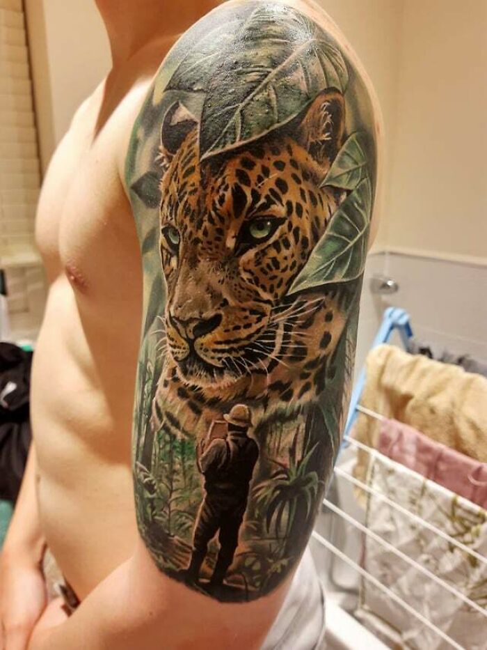 Leopard face in green leaves and a man tattoo on arm 