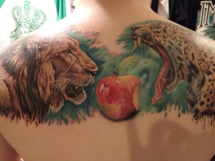 Lion and leopard tattoo on back with a red apple centerpiece, showcasing animal tattoo art.
