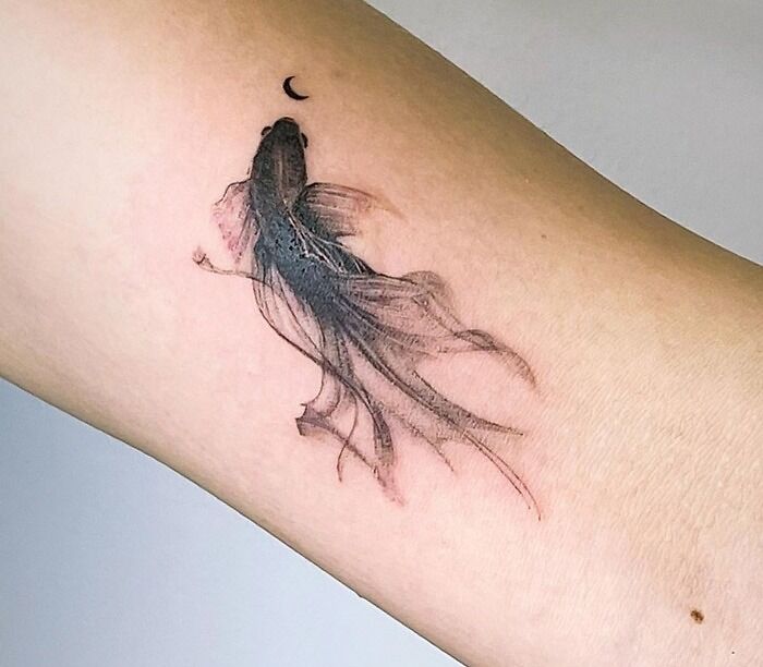 Swimming fish and a little black moon on arm tattoo