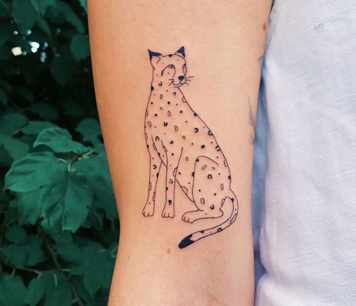 Animal tattoo of a stylized cheetah on a person's arm, featuring minimalist black line art and spots.