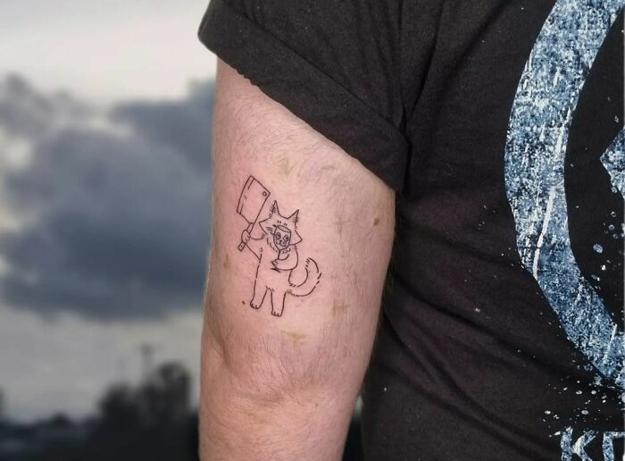Humorous tattoo of a cartoon cat holding a cleaver on a person's arm.