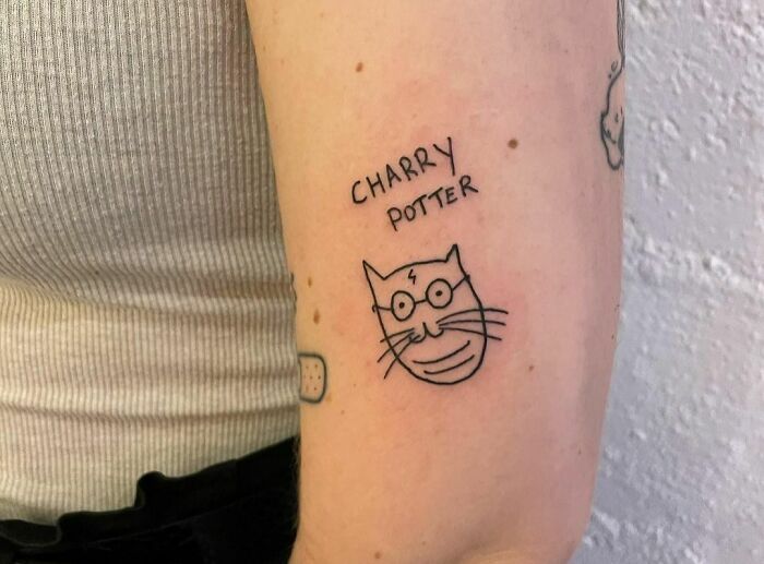 Funny tattoo of a cat with glasses labeled "Charry Potter" on a person's arm.