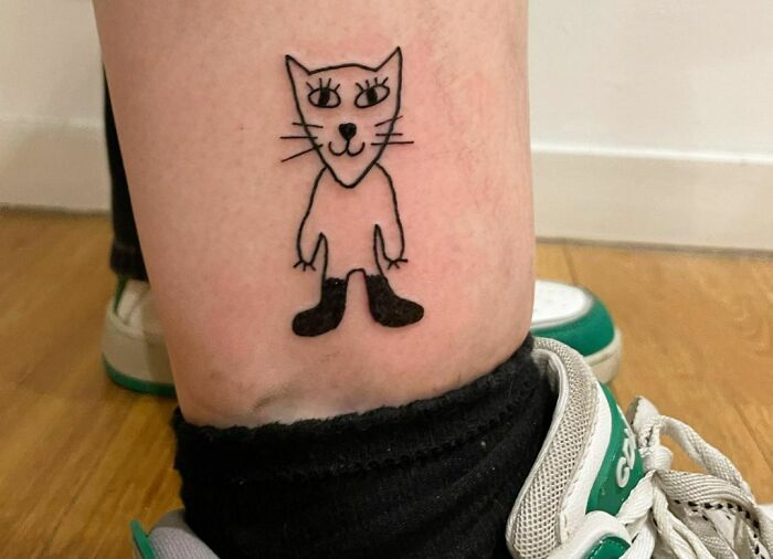 Funny tattoo of a simplistic cat drawing wearing boots on a person's leg.