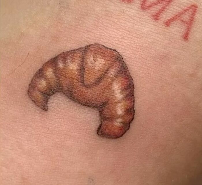 A funny croissant tattoo on skin, designed to evoke a smile.