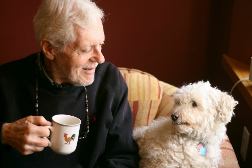 old man with a cup of coffee looking at his dog