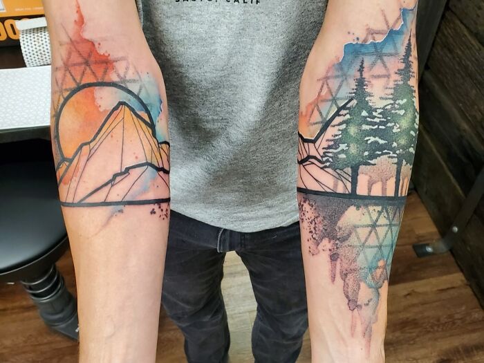 Geometric watercolor tattoos on arms: on one mountains and sun on the other pine tress and mountains