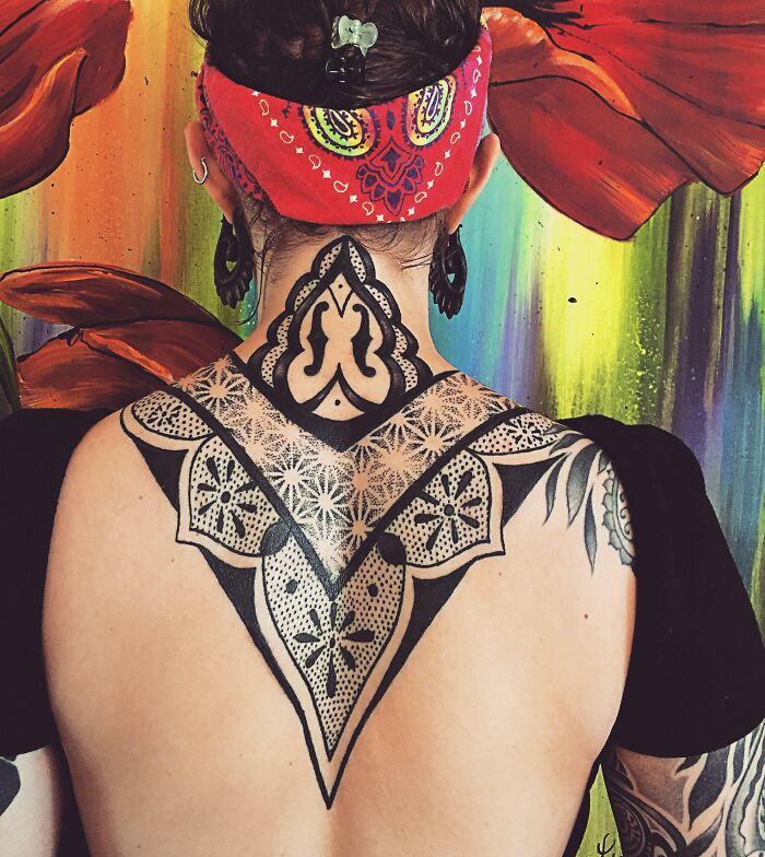 Geometric tattoo on a woman's back, featuring intricate patterns, against a colorful floral background.