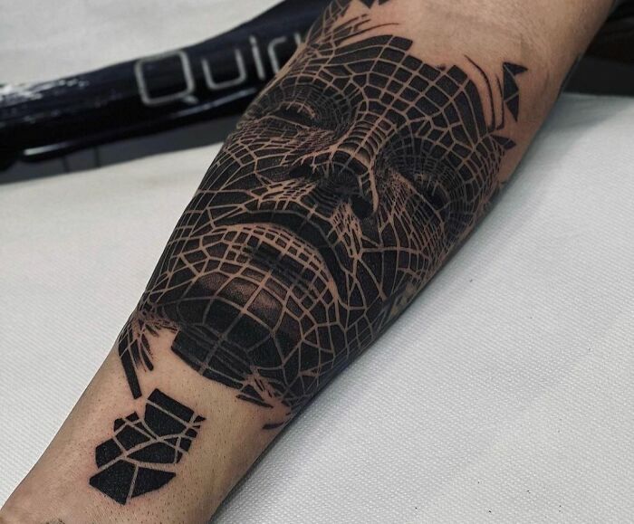 Geometric tattoo of a detailed face design on a forearm, showcasing intricate linework and shading.