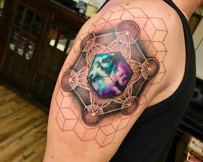 Geometric tattoo with colorful cube and intricate patterns on upper arm.
