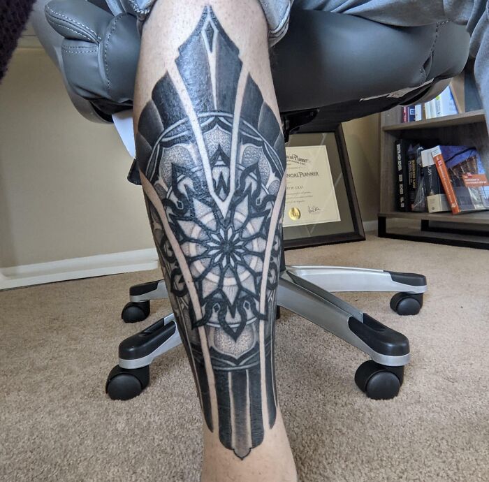 A detailed geometric tattoo on a person’s calf, featuring intricate patterns and bold lines.