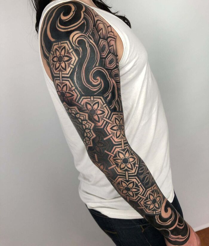 Arm with exquisite geometric tattoo design in black and white patterns on white fabric.