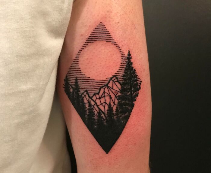 Geometric tattoo with mountains, trees, and a sun on an arm, showcasing intricate black linework.