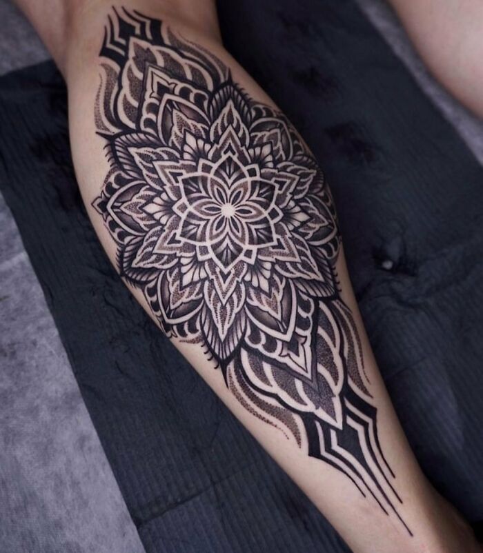 Intricate geometric tattoo on a leg featuring a mandala design with bold, symmetrical patterns.