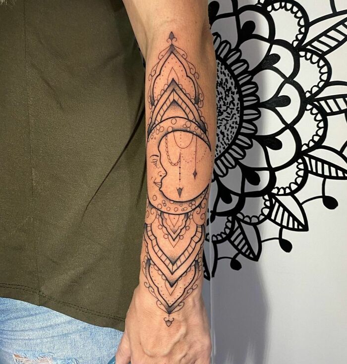 Geometric tattoo with intricate patterns and moon design on a person's forearm, next to a mandala wall art.