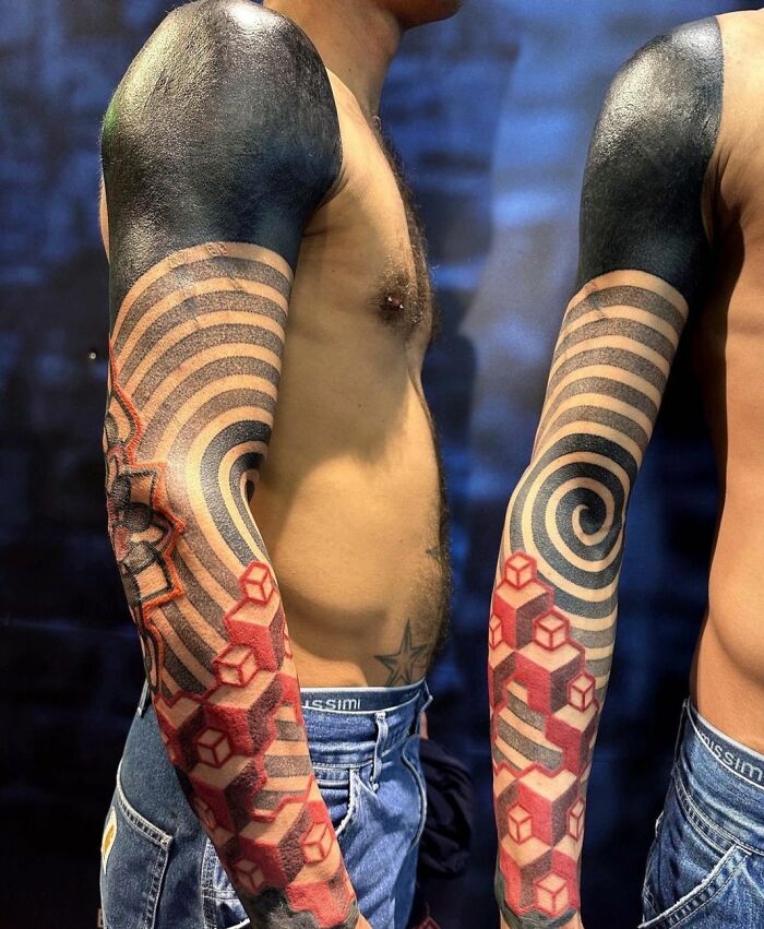 Two arms with intricate geometric tattoos featuring spirals and 3D cubes.