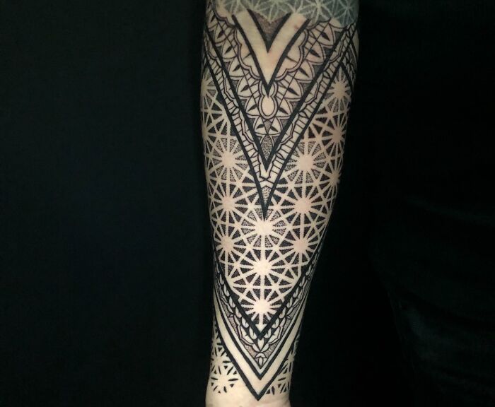 Intricate geometric tattoo design on a forearm, featuring symmetrical patterns and bold lines against a dark background.