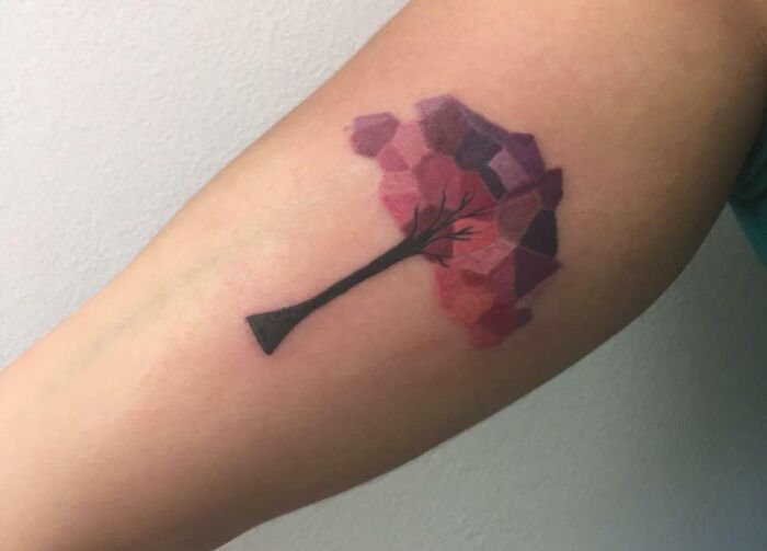 Geometric tattoo of a tree with a colorful polygonal canopy on an arm.