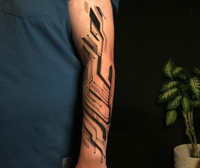 Arm displaying a creative geometric tattoo design with shapes and forms, against a dark background.