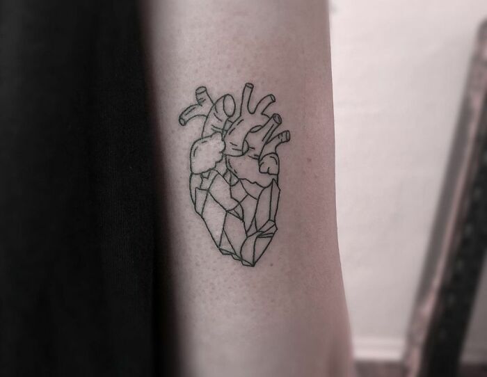 Geometric tattoo of an anatomical heart on an arm, featuring intricate line designs.