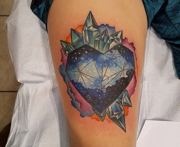 Geometric tattoo of a heart with crystals and galaxy design, featuring vibrant colors on an arm.