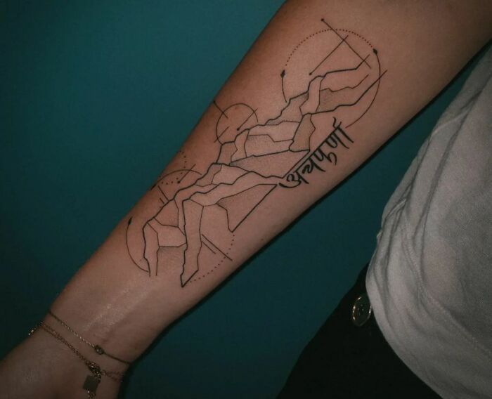 Geometric tattoo on forearm with abstract lines and shapes, featuring a Sanskrit word.