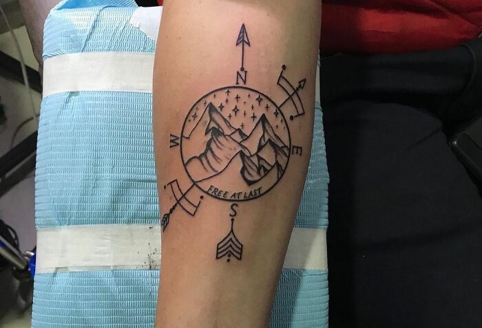Geometric tattoo design featuring mountains and compass with arrows on an arm.